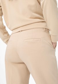 Beige skræddersyede bukser lavet af glat stof, med to baglommer med klapper og et tætsiddende taljebånd.