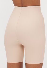 Bežid kõrge vöökohaga lühikesed püksid, mis on tehtud siledast kangast, omavad kehakujulist disaini ja nähtamatuid õmblusi, ulatudes just üle reie.