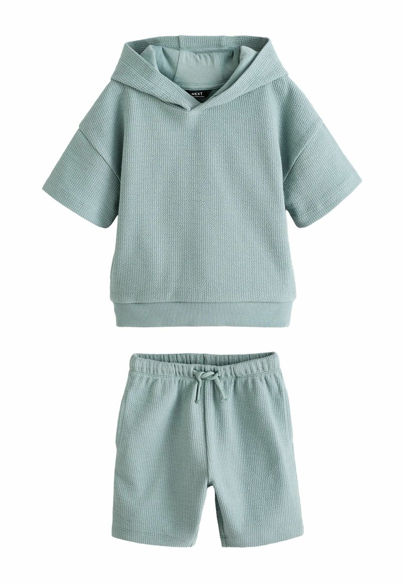 Dvoudílný outfit se světlomodrou strukturovanou mikinou s krátkým rukávem a odpovídajícími kraťasy, obojí vyrobené z měkké, prodyšné tkaniny.