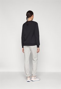 Schwarzer Sweatshirt mit gerippten Bündchen, kombiniert mit hellgrauen Sweatpants mit einer Gesäßtasche, getragen mit grauen und orangefarbenen Sportschuhen.