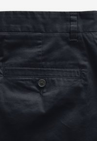Marineblaue Hose mit glatter Textur, Frontreißverschluss und einer Gesäßtasche mit einem runden schwarzen Knopf und gesteppten Details.