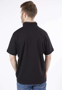 Polo shirt noir avec un col haut et des manches courtes, présentant des rayures d'accent blanches et dorées sur le col et les ourlets des manches.