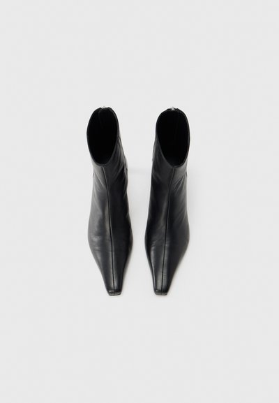 Μαύρα δερμάτινα μποτάκια αστραγάλου με μυτερή μύτη, λεία υφή και φερμουάρ στο πίσω μέρος, που διαθέτουν κομψό και μοντέρνο σχεδιασμό.