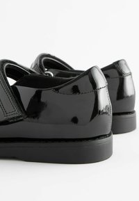 Zapatos de charol negros con un acabado brillante, punta redondeada y un diseño simple. Presentan un ligero tacón y un detalle de costura en contraste.