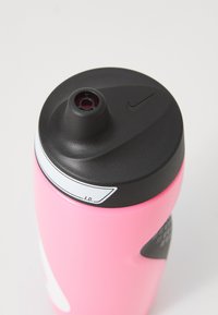 Nike waterfles met een roze body, zwarte deksel en een gestructureerde grip. Bevat een centrale opening met een kleine tuit en een labelsectie.