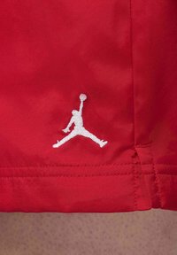 Rote Sportshorts mit glatter Oberfläche, versehen mit einem auffälligen weißen Jumpman-Logo, das auf der linken Seite gestickt ist.