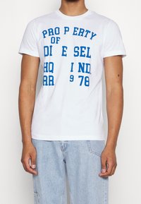 White cotton t-shirt with short sleeves, featuring bold blue text reading "PROPERTY OF DIESEL HQ 1978." Classic crew neck design.
