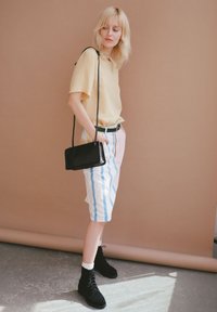 Šviesiai geltona trumpomis rankovėmis marškiniai, pastelinių spalvų dryžuotos šortai mėlynos ir rožinės spalvos, juoda petneša rankinė ir juodi kulkšniniai batučiai su rišamaisiais mazgais.