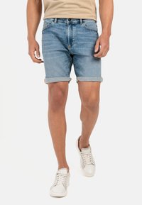 Leren denim shorts in lichtblauw, met opgerolde boordjes, vijf-pocket design en een knoopsluiting. Draagt met witte sneakers.