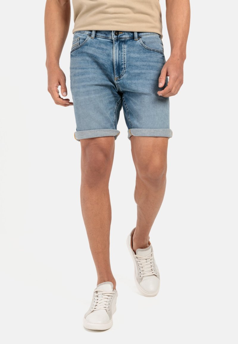 Leren denim shorts in lichtblauw, met opgerolde boordjes, vijf-pocket design en een knoopsluiting. Draagt met witte sneakers.