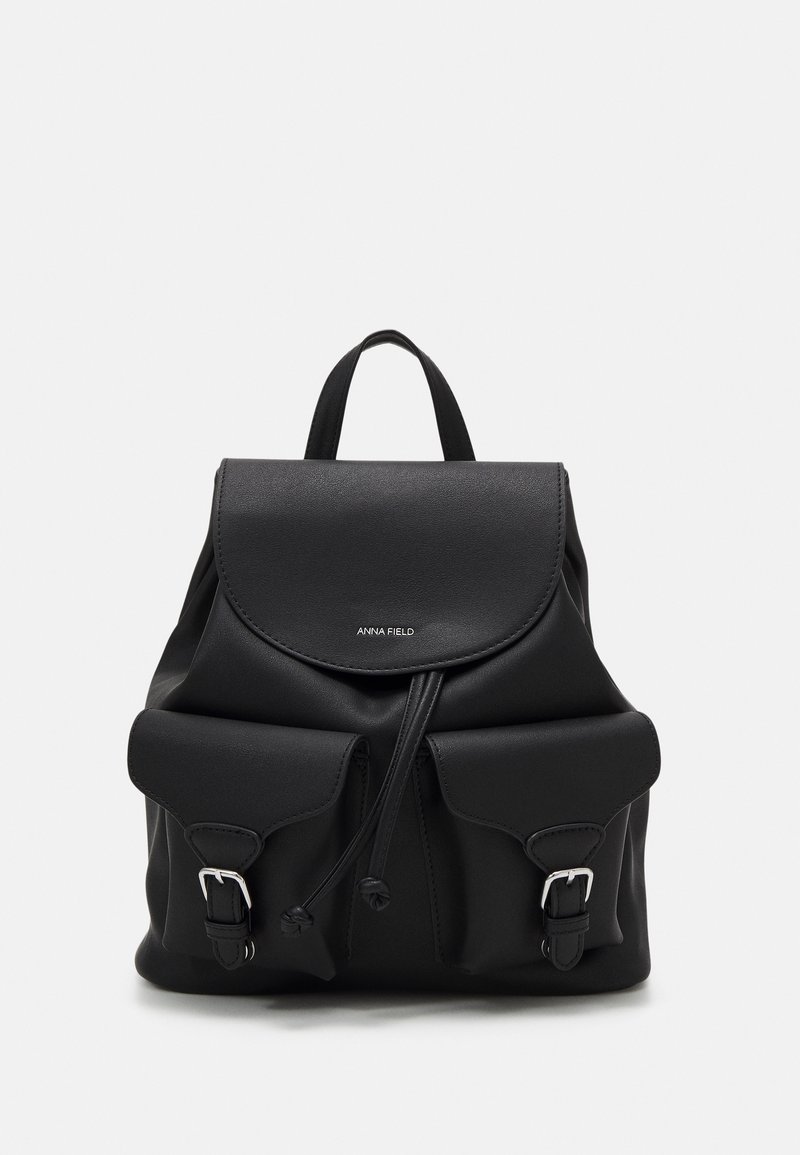Sac à dos en cuir noir avec deux poches avant à boucle, fermeture à cordon, rabat supérieur et une seule poignée.