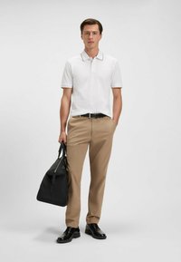 Vit polo med krage och ljusbruna detaljer, beige byxor, svart bälte, svarta skor och en svart handväska.