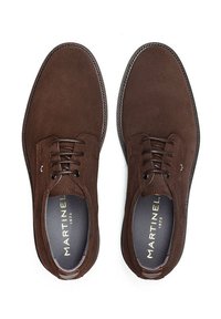 Brązowe zamszowe buty o klasycznym fasonie, z sznurowadłami, teksturowaną powierzchnią i kontrastowym ściegiem wzdłuż podeszwy. Logo producenta widoczne wewnątrz.