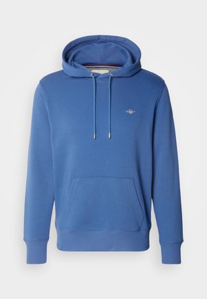 Sininen huppari, jossa on nyörillä säädettävä huppu, etutasku, ribattu hihansuu ja helma, sekä pieni logo rinnassa. Valmistettu pehmeästä puuvillasekoitteesta.