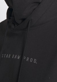 Schwarzer Hoodie aus weichem Material, ausgestattet mit einer Kapuze mit Kordelzug und einem geprägten Text "STAR RAW PROD." über der Brust.