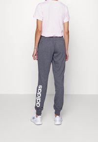 Pantalons de survêtement gris avec un logo "adidas" blanc sur la jambe gauche, associés à un t-shirt rose clair, portés avec des chaussures de sport blanches.