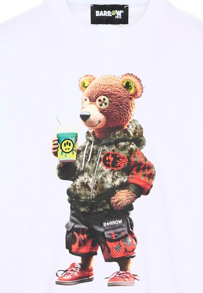 Niedźwiedź w kamuflażowej bluzie z kapturem i szortach z motywem płomieni, trzymający napój z logo smutnej twarzy, w czerwonych trampkach, stojący pewnie.