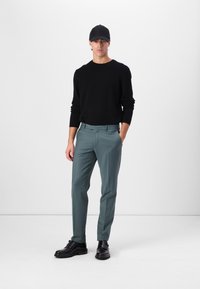 Suéter negro, pantalones de color verde claro, gorra negra y zapatos negros. Diseño ajustado, textura suave y frente plano.