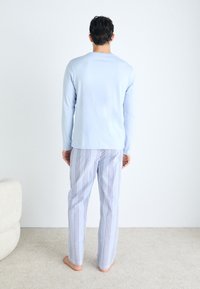 Vaaleansininen pitkähihainen paita yhdistettynä sinivalkoisiin raidallisiin yöpaitahousuihin, jotka esittelevät rentoa istuvuutta ja pehmeää textures. 