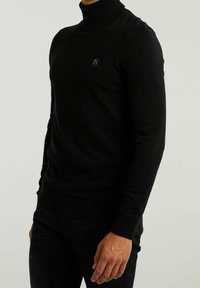Schwarzer Rollkragenpullover mit gerippter Textur und enganliegendem Design. Verfügt über ein kleines Logo auf der Brust sowie gerippte Bündchen und Saum.