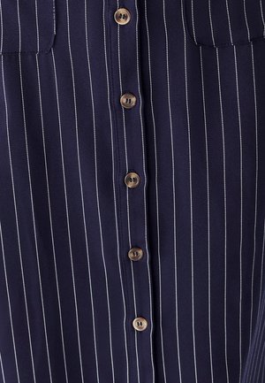 Mornarska košulja na dugih rukava s vertikalnim bijelim prugama, dva džepa na prsima i smeškastim dugmadi duž prednjeg kopčanja.