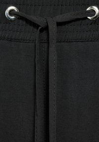 Czarny materiałowy sznurek przewleczony przez srebrne oczka, związany prostym węzłem na elastycznym pasie.