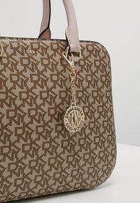 Sac à main DKNY marron et beige à motifs, avec des anses rose pâle et un charm circulaire doré Donna Karan suspendu à la poignée.