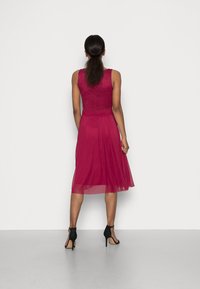 Robe sans manches avec un corsage ajusté en dentelle bordeaux profond, jupe fluide en chiffon, et sandales à talons hauts noires. Vue arrière lisse.