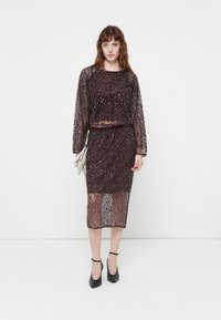 Glinsterende tweedelige outfit in donker bordeaux. Het topje heeft lange mouwen en de rok is tot op de knie. Slanke pasvorm met een gladde textuur.