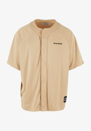 Rövid ujjú, bézs hálós póló kerek nyakkal, elöl gombos záródással, és fekete logóval a bal mellen. Texturált anyag.