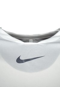 Weißes Sportshirt mit rundem Hals, mit einem schwarzen Nike-Logo auf der Vorderseite. Der Stoff wirkt glatt und körperbetont.