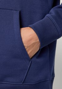 Felpa blu navy con una finitura testurizzata, dotata di una tasca frontale, polsini a coste e dettagli di cucitura visibili.
