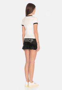 Top corto bianco a maniche corte con bordo nero abbinato a una gonna nera con la scritta "Juicy" in strass e un orlo a volant. Le sneakers bianche completano il look.