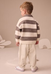 Pull en maille crème à rayures horizontales grises, associé à un pantalon en velours côtelé beige clair et des baskets blanches, vu de dos.