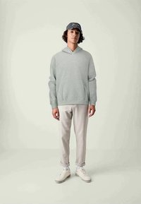 Felpa grigia chiara con cappuccio realizzata in tessuto morbido, vestibilità ampia, polsini a coste, abbinata a pantaloni beige chiaro e sneakers bianche. Cappellino grigio.