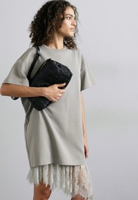 Grey oversized t-shirt dress with short sleeves, featuring a lace bottom trim. The model holds a textured black clutch bag.