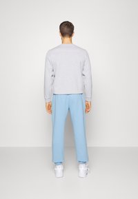 Grå sweatshirt med rund hals, kombinerad med ljusblå sweatpants. Tygerna verkar mjuka, och byxorna har elastiska muddar.