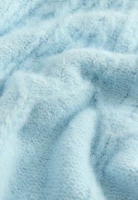 Šviesiai mėlyna mezginė medžiaga su minkštu, pūkuotu paviršiumi, kuriame derinami įvairūs ornamentai ir siūlės, sukuriantys gylį ir vizualinį susidomėjimą.