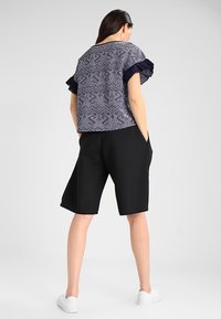 Czarne szorty z kieszeniami w połączeniu z granatową bluzką w wzory, posiadającą falbaniaste rękawy i luźny krój. Widoczne detale z teksturowanej tkaniny.