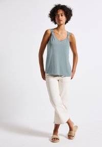 Ljusblå ärmlös topp med V-ringning, prydd med dekorativa band vid axlarna. Matchas med krämfärgade, korta byxor och vävda sandaler.