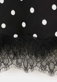 Tissu noir à pois blancs avec une délicate bordure en dentelle florale noire sur le bord.