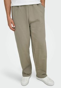 Jasnoszare, luźne spodnie dresowe z elastycznym paskiem w talii, bocznymi kieszeniami i miękką fakturą. W połączeniu z białymi trampkami.