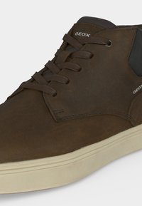 Baskets en cuir marron Geox avec lacets marron foncé et semelle en caoutchouc blanche, avec des détails cousus et un col de talon rembourré noir.