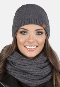 Berretto in maglia grigia con un motivo testurizzato e un'etichetta in pelle, abbinato a una sciarpa in maglia grigia coordinata, entrambi caratterizzati da un aspetto caldo e morbido.