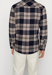 Koszula w kratę w kolorach granatowym, beżowym i czerwonym. Posiada długie rękawy, mankiety na guziki oraz zaokrąglony dół. Miękka, teksturowana tkanina.