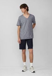 T-shirt gris à col en V et manches courtes, associé à un short en jean foncé. Le mannequin porte des chaussettes blanches jusqu'à la cheville et des baskets claires.