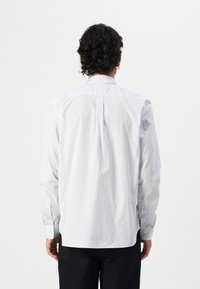 Camisa blanca de vestir con rayas verticales azules, de manga larga, con puños abotonados y un pliegue en la parte posterior. La tela es suave y ligera.