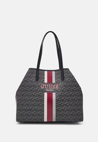 Torba tote z ciemnoszarym wzorem geometrycznym, pionowymi czerwonymi i białymi paskami oraz wytłoczonym logo "GUESS EST. 1981" z przodu. Czarne uchwyty.