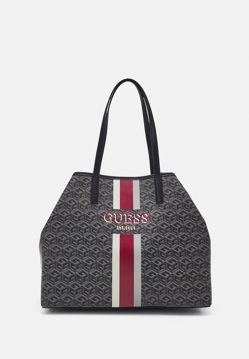 Torba tote z ciemnoszarym wzorem geometrycznym, pionowymi czerwonymi i białymi paskami oraz wytłoczonym logo "GUESS EST. 1981" z przodu. Czarne uchwyty.
