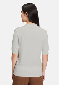 Jasnoszara bluzka z krótkim rękawem, okrągłym dekoltem i żebrowanym wykończeniem. Materiał wydaje się miękki i gładki w dotyku. Prosty, minimalistyczny design.